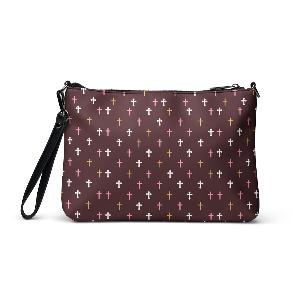 the front of a deep plum crossbody bag with white, pink, and gold crosses patterned all over. wrist strap on left side of bag. 
