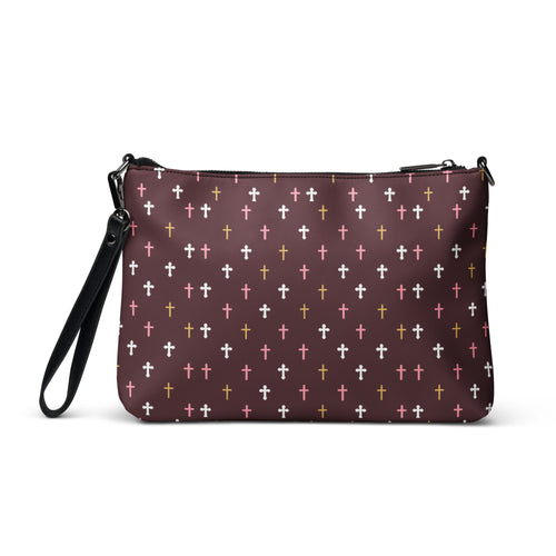 the front of a deep plum crossbody bag with white, pink, and gold crosses patterned all over. wrist strap on left side of bag. 