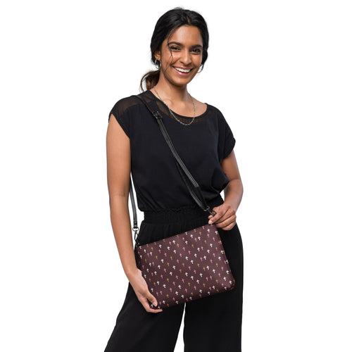 woman wearing aa deep plum crossbody bag with white, pink, and gold crosses patterned all over. cross body strap over her right shoulder 