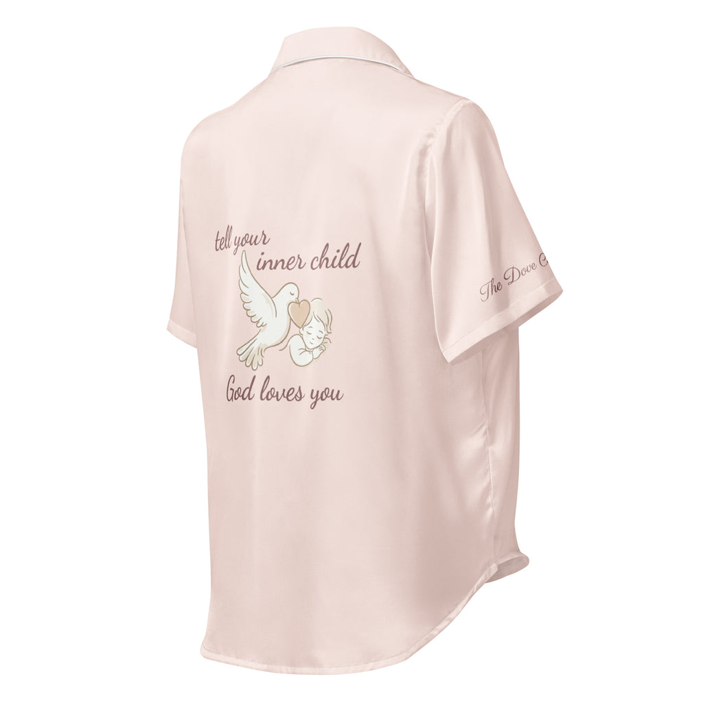 Pink silk pajama shirt with text that reads "tell your inner child God loves you" and dove graphic on a white background