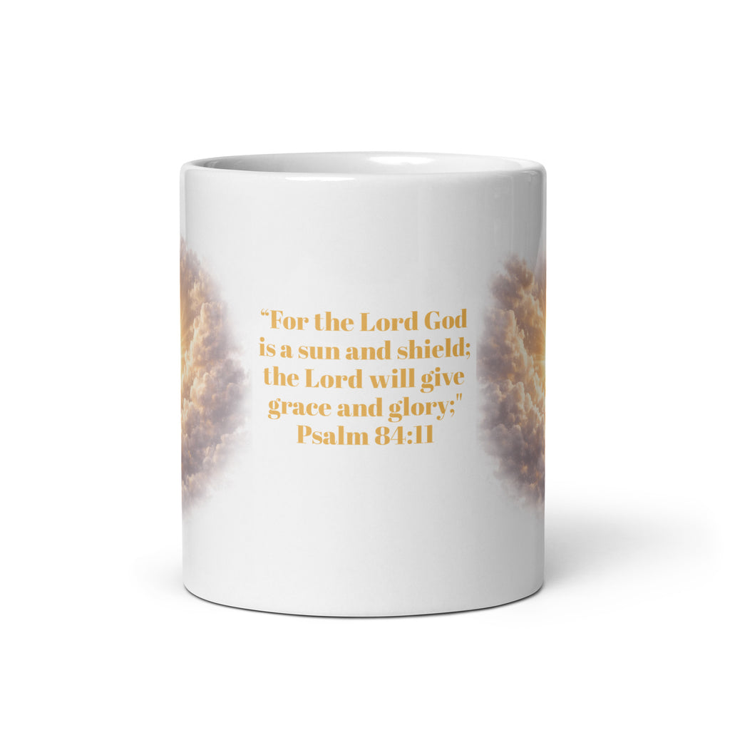 white ceramic mug featuring a golden scripture quote that reads, "For the Lord God is a sun and shield; the Lord will give grace and glory. Psalm 84;11" with radiant clouds and sunlight artwork wrapping around the sides. 